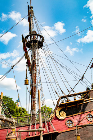 Low-angle shot of a pirate ship mast against a blue sky with white clouds, focusing on rigging,...