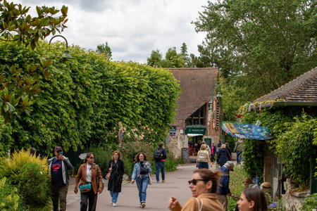A street scene with tourists walking past a cafÃ© and lush greenery under a cloudy sky in Giverny, France.の写真素材