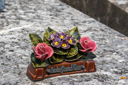 Ceramic floral grave marker features stylized roses and violets on a brown base with inscription "AndrÃ© Grand-MÃ¨re" set on a weathered stone surface in Giverny, France.の写真素材