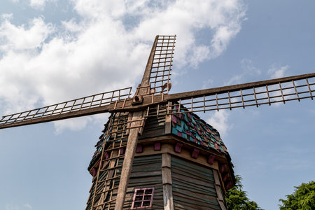 A low-angle shot of a wooden windmill with colorful shingles, set against a bright sky with white clouds. The windmill is the dominant element.の写真素材