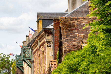 Close-up of buildings featuring brickwork, roofs, and French flags. Green foliage frames the right side of the image in Giverny, France.の写真素材