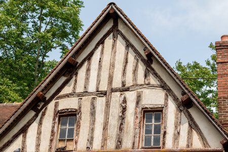 Close-up of a building's gable end, showcasing half-timbered construction and aged materials against a backdrop of trees and sky in Giverny, France.の写真素材