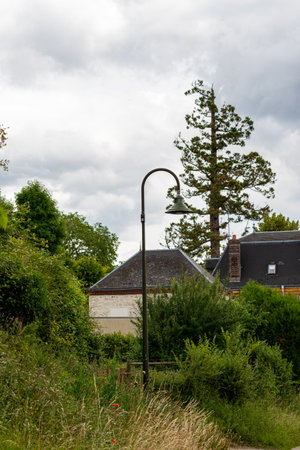 A street lamp stands amidst greenery, with building rooftops visible in the background under a cloudy sky in Giverny, France.の写真素材