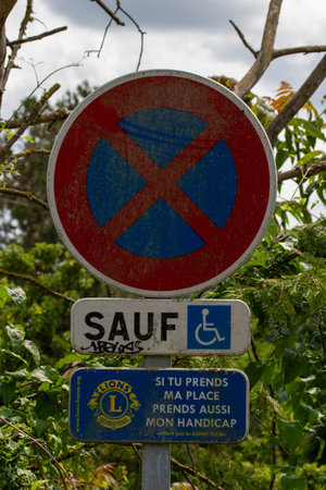 A layered parking sign with "no parking," handicapped exceptions, and a Lions Club message, surrounded by foliage in Giverny, France.の写真素材