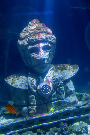 Underwater view of an ancient stone statue, featuring fish swimming nearby, set against a deep blue background.の写真素材