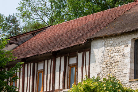 Exterior shot of a building featuring a tiled roof, half-timbered wall, and stone facade, surrounded by greenery in Giverny, France.の写真素材