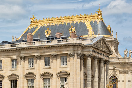 Detailed architectural shot of a section of the Palace of Versailles, featuring its ornate roof and facade, against a partly cloudy sky.の写真素材