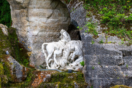 White marble sculpture of men and horses situated within a rock structure with moss and greenery at Versailles Gardens, Paris.の写真素材