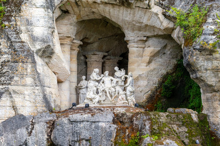 Sculpture of figures within a grotto. Rough, textured rock and vegetation surround the sculpture, with built in columns at Versailles Gardens, Paris.の写真素材