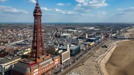 Aerial view of a seaside town with a prominent red iron tower, a wide promenade, a beach, and densely packed buildings  in Blackpool, UK.の写真素材