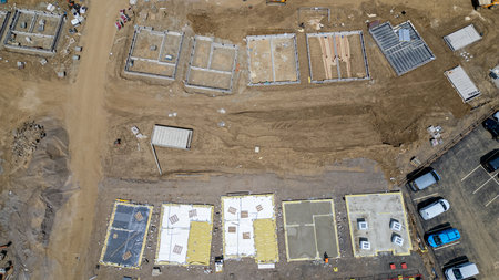 Aerial view of a construction site with multiple foundations, concrete slabs, and building materials scattered across the dirt and gravel terrain.の写真素材