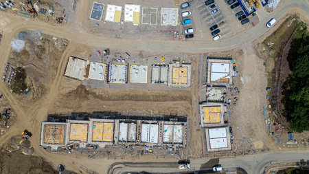 Aerial view of a construction site with multiple building foundations and early-stage structures, vehicles, and materials.の写真素材