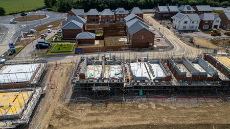 Aerial view of a residential construction site with new homes in various stages of development, featuring unfinished foundations and brickwork alongside completed houses.の写真素材