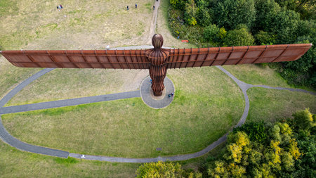 Aerial view of the rusty metal Angel of the North sculpture, spread across a green grassy landscape with winding paths and surrounding trees  in Newcastle upon Tyne, UK.の写真素材