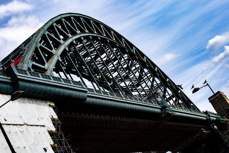 A low-angle view of a steel arch bridge with a complex lattice structure against a bright blue sky with wispy clouds  in Newcastle upon Tyne, UK.の写真素材