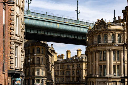 An urban scene featuring a large, teal-colored bridge spanning over ornate, stone buildings under a partly cloudy sky  in Newcastle upon Tyne, UK.の写真素材