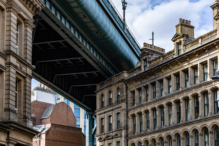 A large green bridge spans over historic stone buildings and brick structures under a cloudy sky.の写真素材