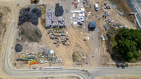 Aerial view of a construction site with piles of materials, building supplies, vehicles, and a small hexagonal structure.の写真素材