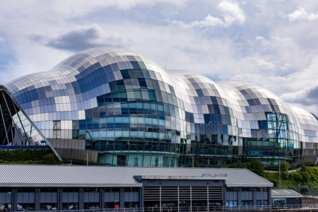 A modern, curved building with a distinctive tiled facade of silver, white, and blue panels, reflecting the cloudy sky  in Newcastle upon Tyne, UK.の写真素材
