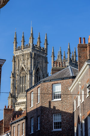 A detailed gothic tower with ornate carvings and spires stands behind brick buildings with...