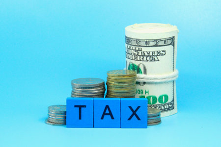 a roll of paper money, a coin and the word TAX on a blue wooden boxの写真素材