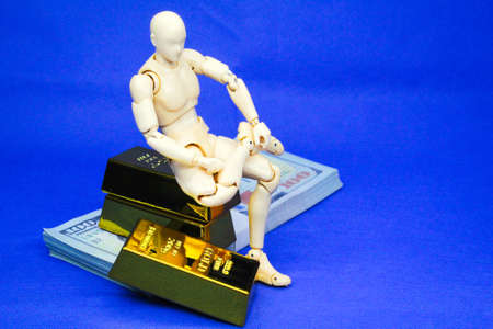 The connected male wooden mannequins sit on gold and money ingots. asset conceptの写真素材