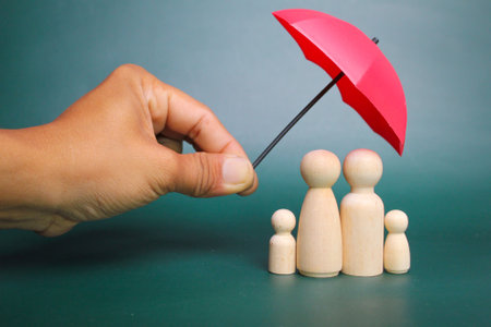 a family of wooden figures protected by a yellow umbrella. Family care, protection and insurance concept.の写真素材