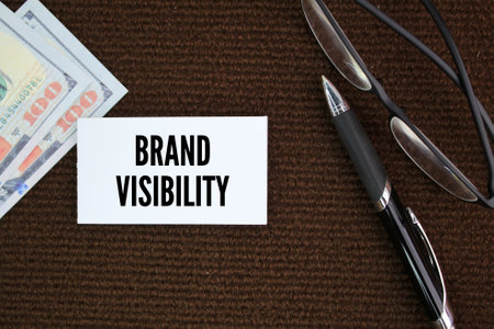 glasses, pens and paper money with the word Brand visibility. Business and Brand visibility concept. own brand conceptの写真素材