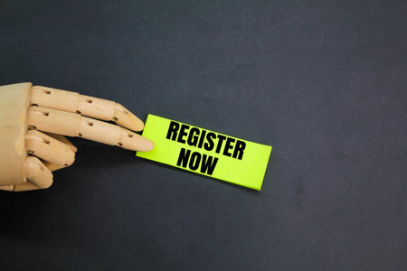 wooden hand and colored paper with the words Register now. REGISTER NOW concept