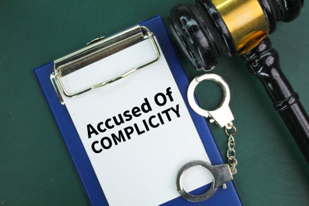 iron handcuffs, a judge's hammer and a paper board with the words accused of complicity. the concept...