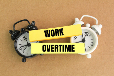 two clock bells and colored paper with the word work overtime. the concept of work exceeds timeの写真素材