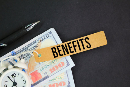 pen, paper money, bell clock and paper tag with the word benefits. the concept of benefit or profitの写真素材