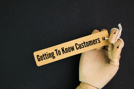 hand and a wooden tag with the words getting to know customers. customer or buyer conceptの写真素材