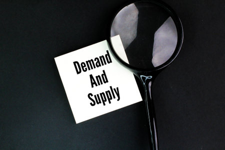 magnifying glass and white paper with the words demand and supply. the concept of high demand in the marketの写真素材