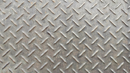 Metal or sheet metal background, steel plate surface texture. A close-up of a metallic, diamond plate texture with a raised, repeating pattern. The surface appears worn and slightlの写真素材