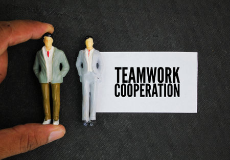 two miniature people and paper with the word teamwork cooperation. the ability to work cooperatively...