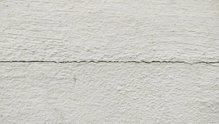 a line of cracks in the cement wall. broken white wall background. textured cement wall with a visible horizontal crack running across its surface. The crack is thin but noticeableの写真素材