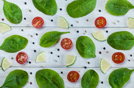 Still life food photo with spinach leaves, lime, cherry tomatos and thyme on white wooden rustic background. Colorful artistic food pattern. Vegetable and greens collage top view.の写真素材
