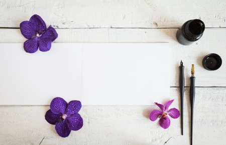 Empty sketchbook on wooden desk with orchid flowers around. Mockup for elegant design.