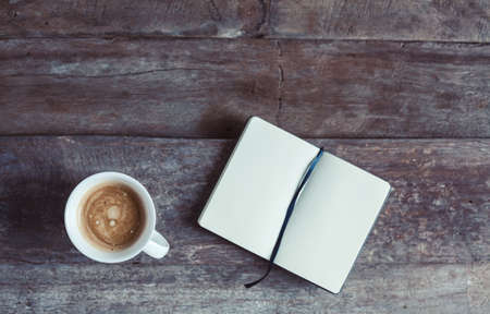 Cup of coffee and notebook with blank pages on a wooden background - photo taken from the top. Metaphor of a creative process.の写真素材