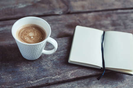 Cup of coffee and notebook with blank pages on a wooden background - photo taken from the top. Metaphor of a creative process.の写真素材