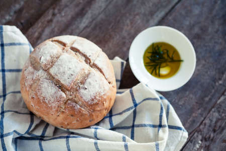 Close up photo of fresh baked bread on rustic wooden background with shallow depth of field. Olive oil with rosmarine and garlic on the side.の写真素材