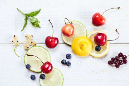 Top view photo of lemon, lime, cherry, red and white currant and blueberries on white wooden table....