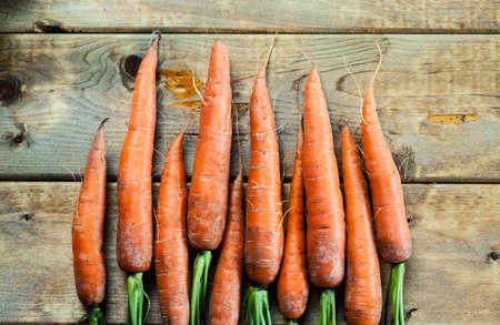 Fresh farm grown young carrots served whole on an old rustic wooden table for healthy vegetarian fare. Overhead view.の写真素材