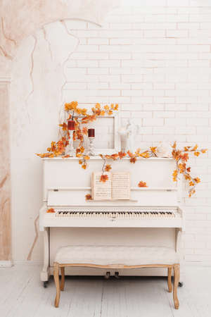 White piano decorated with yellow leaves in front of old white brick wall. Autumn season in photo studio.の写真素材