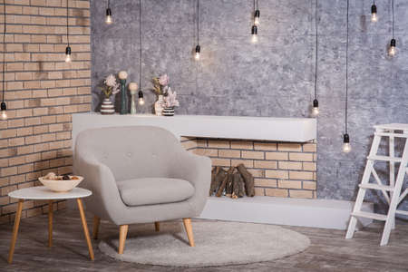 Interior of scandinavian style: contemporary fireplace with firewood, cozy armchair and coffee table. Garland of bulbs hanging from the ceiling.の写真素材