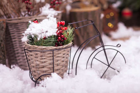 Small decorative bicycle with wicker basket, which contains Christmas tree branches and red winter berries, stands in the middle of snowflake. Festive backgroundの写真素材