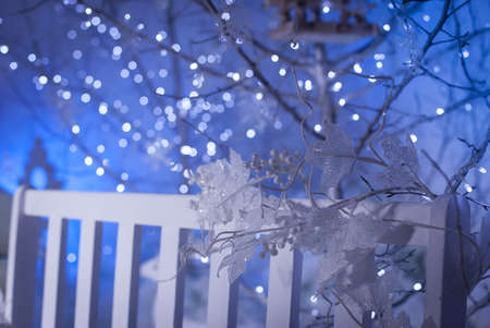white frozen leaves and berries entwine bench in winter yard. Silver tree with New Year garland at the background. Christmas decorationの写真素材