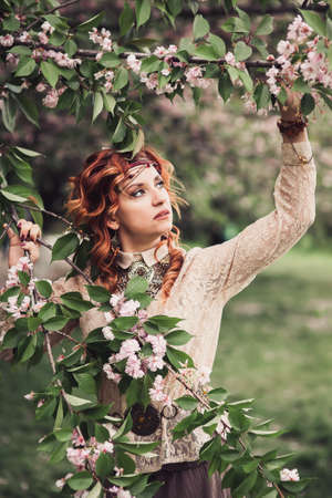 Beautiful hippie woman enjoying garden, pretty girl relaxing outdoor, holding branch, young lady and spring green nature, romantic conceptの写真素材
