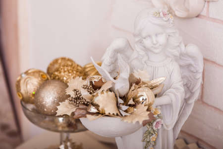 Angel statuette holding a bowl with golden Christmas ornaments and leaves. Close-upの写真素材